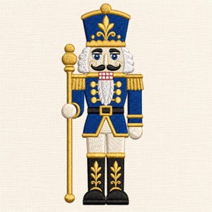 Könnte beinhalten: Eine Stickerei eines Nussknackers in einer blauen Uniform mit goldenen Verzierungen, einem hohen blauen Hut mit goldener Lilie und schwarzen Stiefeln. Die Figur hat einen weißen Bart, einen schwarzen Schnurrbart und hält einen goldenen Stab.