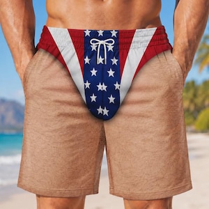 May include: Swim trunks featuring a tan skin-tone base color with a central vertical panel displaying a blue background with white stars, flanked by white and red diagonal stripes at the waistband, complete with a white drawstring closure.
