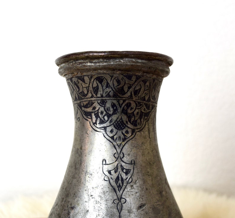 May include: A silver pitcher with intricate black floral designs etched into the surface.
