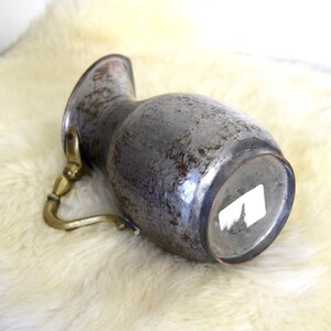 May include: A vintage copper pitcher with a brass handle. The pitcher has a worn, distressed finish and is a light gray color.