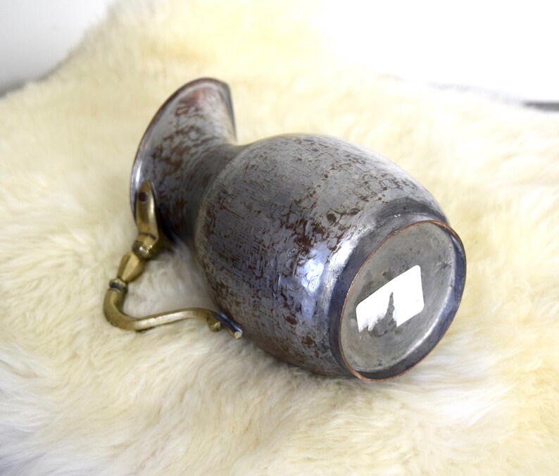 May include: A vintage copper pitcher with a brass handle. The pitcher has a worn, distressed finish and is a light gray color.