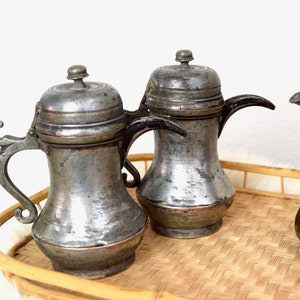 May include: Three antique silver teapots with ornate handles and lids on a woven bamboo tray.