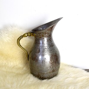 May include: A silver pitcher with a hammered finish and a brass handle. The pitcher is sitting on a white faux fur rug.
