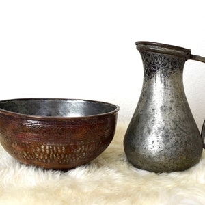 May include: A set of two antique copper bowls, one with a hammered finish and the other with an engraved design. The bowls are sitting on a white faux fur rug.
