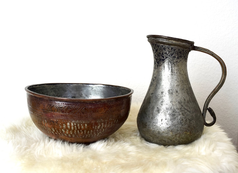 May include: A set of two antique copper bowls, one with a hammered finish and the other with an engraved design. The bowls are sitting on a white faux fur rug.