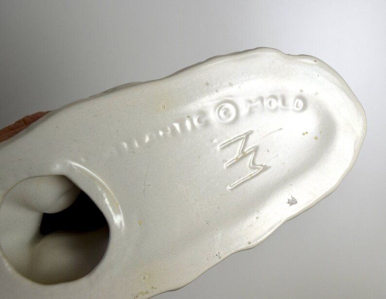 May include: White ceramic figurine with a brown base. The bottom of the figurine is marked "Plastic &copy; Holo" and a stylized "Z" logo.