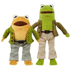 May include: Two plush frog figures standing side by side. The left frog is tan with a green checkered jacket and gray pants. The right frog is green with a solid olive jacket, a brown belt, and beige pinstriped pants. Both have wide mouths.