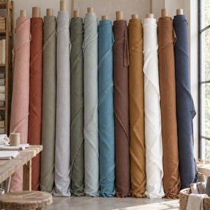 May include: A collection of twelve vertical fabric rolls arranged in a row, featuring a diverse palette of colors including dusty pink, terracotta, sage green, light gray, olive, pale blue, teal, dark brown, mustard yellow, white, tan, and navy blue.
