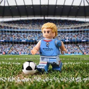 Pode incluir: Uma minifigura de plástico vestindo uma camisa de futebol azul claro do Manchester City com o logotipo da Etihad Airways e o número 9 nos calções. A figura tem cabelo loiro e está posicionada num campo de relva verde junto a uma bola.