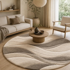 May include: A large circular area rug featuring a textured, wave-like pattern in alternating shades of cream, beige, and dark brown. The rug has a soft, plush pile and is positioned on a light-coloured wooden floor in a living room setting.