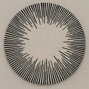 May include: A circular rug featuring a light beige base color with a black sunburst pattern radiating from the center toward the outer edges. The design consists of numerous thin, vertical black lines of varying lengths that create a starburst effect.
