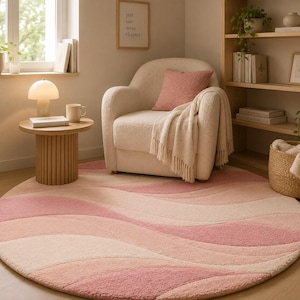 Puede incluir: Una alfombra redonda con un patrón abstracto ondulado en varios tonos de rosa, crema y melocotón suave. La alfombra tiene una superficie texturizada y afelpada, y está colocada sobre un suelo de madera clara en una habitación con un sillón.