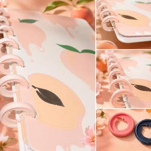 May include: A disc-bound notebook featuring a white cover with a repeating peach pattern, including light pink fruit shapes and dark green leaves. The notebook uses light pink plastic discs for binding. Two separate discs in pink and dark blue are shown.