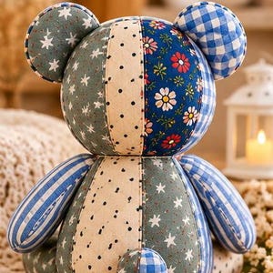 May include: A patchwork teddy bear constructed from various fabric patterns including blue and white gingham, sage green with white stars, cream with black polka dots, and a dark blue floral print with red and white daisies, featuring round ears.