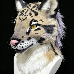 May include: A realistic feline animal head mask featuring tan fur with black spots and stripes, bright yellow eyes, a pink nose, and long white whiskers. The mask includes a thick white chest ruff and a long, flowing light purple mane.