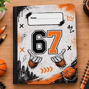 Puede incluir: Un cuaderno rectangular con una cubierta blanca que presenta un diseño gráfico en negro y naranja. La cubierta muestra el número 67, dos manos de dibujos animados, un balón de baloncesto, un horizonte urbano y un campo de nombre con el texto Name:.