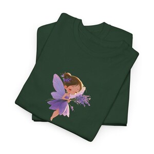 May include: A dark forest green t-shirt featuring a graphic illustration of a small fairy with brown hair, wearing a purple dress and wings, holding a bouquet of lavender flowers. The fairy has closed eyes and a peaceful expression on its face.