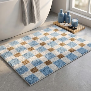 Puede incluir: Una alfombra de baño rectangular con un patrón de cuadros repetitivo en azul claro, blanco y bronceado. La alfombra tiene una construcción de pelo grueso, texturizado y peludo con un borde acabado, diseñada para el suelo del baño.
