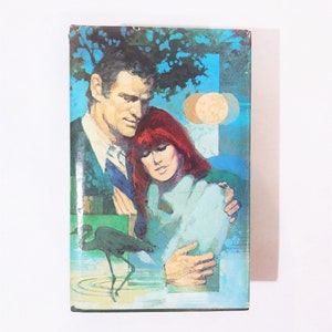 May include: A vintage paperback book cover featuring a couple embracing, with a blue and green background and a bird in the foreground.