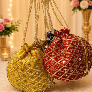 Puede incluir: Dos bolsas con cordón, una amarilla y otra roja, con un patrón de celosía dorada con espejos circulares incrustados y abalorios. Cada bolsa tiene un asa larga hecha de cuentas blancas tipo perla, y la tela tiene un brillo satinado.