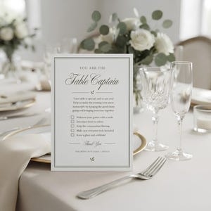 Könnte beinhalten: Eine weiße rechteckige Karte mit schwarzem Rand und dem Text: YOU ARE THE Table Captain. Die Karte enthält eine Checkliste mit Aufgaben für Gäste und endet mit Thank You FOR BEING OUR TABLE CAPTAIN, platziert auf einem gedeckten Tisch.