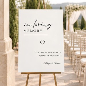 May include: A white rectangular sign on a gold easel featuring the black text "in loving MEMORY" followed by a horizontal line, a small heart icon, the text "FOREVER IN OUR HEARTS, ALWAYS IN OUR LIVES." and the script text "Always & Forever".