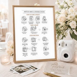 May include: A framed instructional sign for an Instax Mini 12 camera with black text and line drawings on a white background, placed next to a white instant camera, a stack of small square photographs, and a clear acrylic photo guestbook sign.