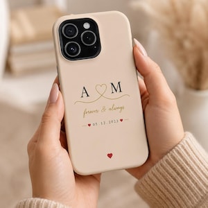 Peut inclure: Une coque de smartphone beige avec les lettres noires A et M séparées par un contour de cœur doré. En dessous, le texte forever & always est écrit en lettres dorées, suivi de la date 05.12.2023 entre deux petits cœurs rouges et un cœur rouge.
