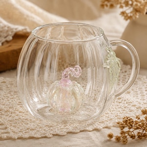 Peut inclure: Une tasse en verre transparent avec un corps arrondi et nervuré en forme de citrouille. À l'intérieur de la tasse, une petite citrouille en verre irisé rose et blanc repose sur la base. Une feuille en verre vert pâle est fixée à l'extérieur.