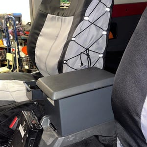 Może przedstawiać: Czarno-szary pokrowiec na fotel samochodowy z systemem sznurowania na elastycznej lince z boku oraz logo Ironman 4x4. Ciemnoszary schowek konsoli środkowej znajduje się między siedzeniami, obok czarnego elektronicznego radia.