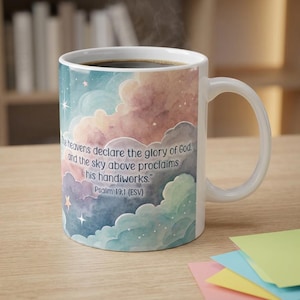 May include: A white ceramic mug featuring a watercolor-style sky design with pastel clouds in shades of blue, pink, and purple. The text reads: The heavens declare the glory of God, and the sky above proclaims his handiworks. Psalm 19:1 (ESV).