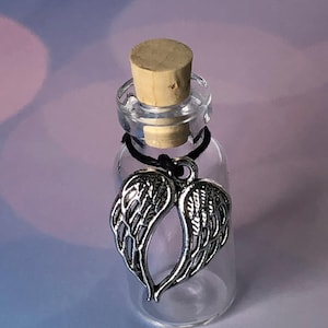 May include: A small, clear glass bottle with a cork stopper and a silver-colored angel wing charm. The charm is attached with a black cord. The background is a soft gradient of purple and white.