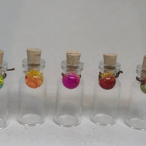 May include: Six small glass bottles with cork stoppers and colorful round charms. The charms are green, orange, pink, red, and two shades of green.