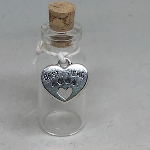 May include: A small glass bottle with a cork stopper and a silver heart charm that says "Best Friend" hanging from it.
