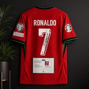 Puede incluir: Una camiseta de fútbol roja con el nombre RONALDO y el número 7 en blanco en la parte posterior. El número 7 incluye una firma negra. Tiene parches en ambas mangas, un cuello negro y verde, y un certificado de autenticidad rectangular.