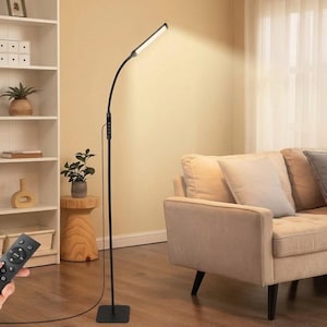 May include: A tall, slender black floor lamp with a flexible neck and a rectangular LED light head emitting a warm glow. The lamp features a control panel on the pole and is operated by a handheld remote control with multiple circular buttons.