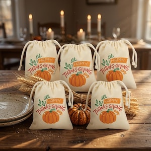 以下が含まれることがあります： オレンジ色のカボチャのグラフィックと「Happy Thanksgiving」の文字がプリントされた、クリーム色の巾着袋5枚。木製のテーブルの上に小麦の穂と小さな本物のカボチャと一緒に配置されており、背景にはぼやけたキャンドルが見える。