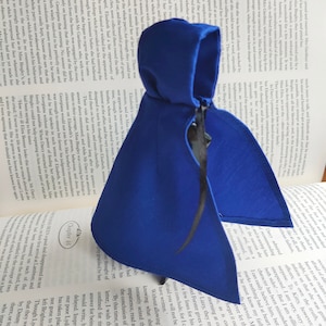 May include: A dark blue hooded cloak, likely for cosplay or costume use, with a flowing design. The cloak is draped over an open book, suggesting a literary or historical theme.