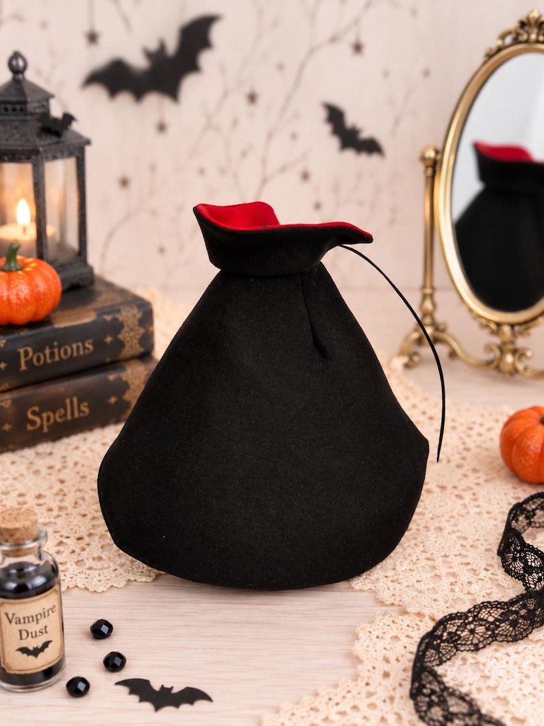 May include: A black drawstring pouch with a vibrant red interior lining. The bag features a wide, rounded base that tapers toward the top opening, which is cinched with a thin black cord. The exterior fabric has a soft, matte texture.
