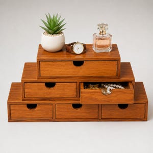 May include: A tiered wooden desk organizer with six drawers arranged in a pyramid shape. The top level has one drawer, the middle has two, and the bottom has three. A small succulent, a wristwatch, and a glass perfume bottle sit on top.