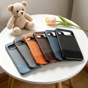 May include: A collection of six rectangular phone cases arranged in a fan shape, featuring textured surfaces in shades of light blue, gray, orange, brown, dark blue, and black, each with a smooth solid-colored base section and a cutout at the top.