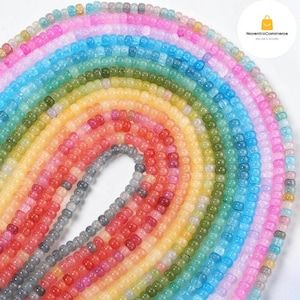 May include: A collection of translucent, multi-coloured pony beads arranged in a circular, rainbow-like gradient pattern. The beads feature a smooth, glossy finish and are displayed in concentric rows, showcasing shades of pink, blue, green, yellow, and grey.