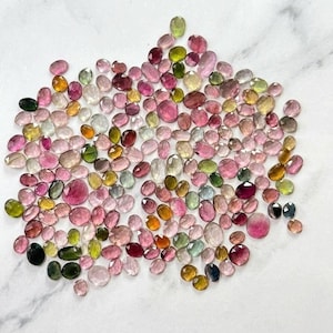 Può includere: Una vasta collezione di pietre preziose sfaccettate sciolte di varie forme e dimensioni. Le pietre presentano un ampio spettro di colori, tra cui sfumature di rosa, magenta, verde, giallo e trasparente, con finitura lucida e riflettente.