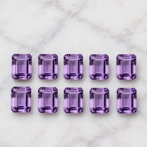 Könnte beinhalten: Zehn lose Amethyst-Edelsteine im Smaragdschliff, angeordnet in zwei horizontalen Reihen zu je fünf Stück. Jeder Edelstein hat einen leuchtenden, durchscheinenden violetten Farbton mit einer facettierten Oberfläche, die das Licht reflektiert.