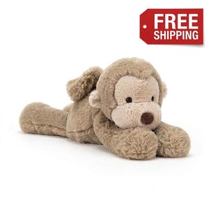 May include: A plush monkey toy made of soft, light brown fur. The stuffed animal is in a lying position with its head raised, featuring a lighter beige face, small round ears, dark eyes, and a dark brown nose. The texture is fuzzy and soft.