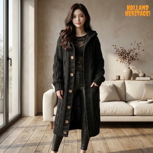 May include: A long black cable-knit hooded cardigan featuring a front button closure with light brown buttons, worn over a black lace top and black trousers. The text HOLLAND HERITAGE is visible in the upper right corner of the image.