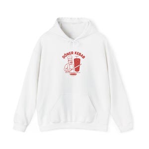 Könnte beinhalten: Ein weißer Kapuzenpullover mit einem roten Grafikdruck auf der Brust. Das Motiv zeigt einen Koch mit Schnurrbart und Kochmütze, der ein Messer neben einem vertikalen Drehspieß hält, mit dem Text DÖNER KEBAB über der Figur.