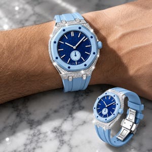 May include: A light blue wristwatch featuring a dark blue textured dial with a small sub-dial, a silver-toned bezel and case encrusted with clear stones, and a light blue rubber strap with a silver-toned metal deployment clasp mechanism.