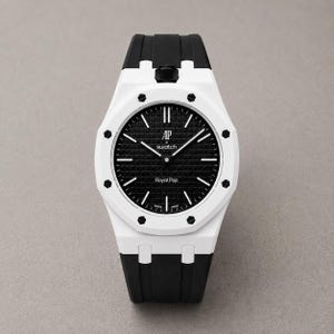 Puede incluir: Un reloj de pulsera con bisel octogonal blanco y tornillos hexagonales negros, esfera negra texturizada con marcadores de hora blancos y el texto AP x swatch y Royal Pop. El reloj cuenta con una correa de silicona negra y caja blanca.