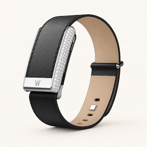 May include: A black leather fitness tracker band featuring a silver-toned rectangular module with a pavé crystal side panel and a prominent letter W engraved on the front metal clasp. The strap has a smooth black exterior and a light beige interior lining.